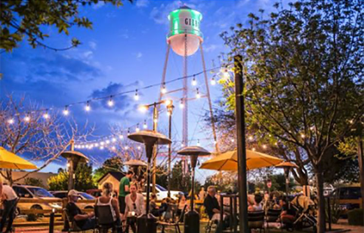 A group of people are sitting at tables at night near a water tower.